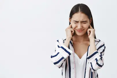 Daughter covering ears being displeased of loud fight of parents, feeling intense and timid. Portrait of unhappy and sad cute woman in blouse, frowning with closed eyes trying not hear noise. Copy space