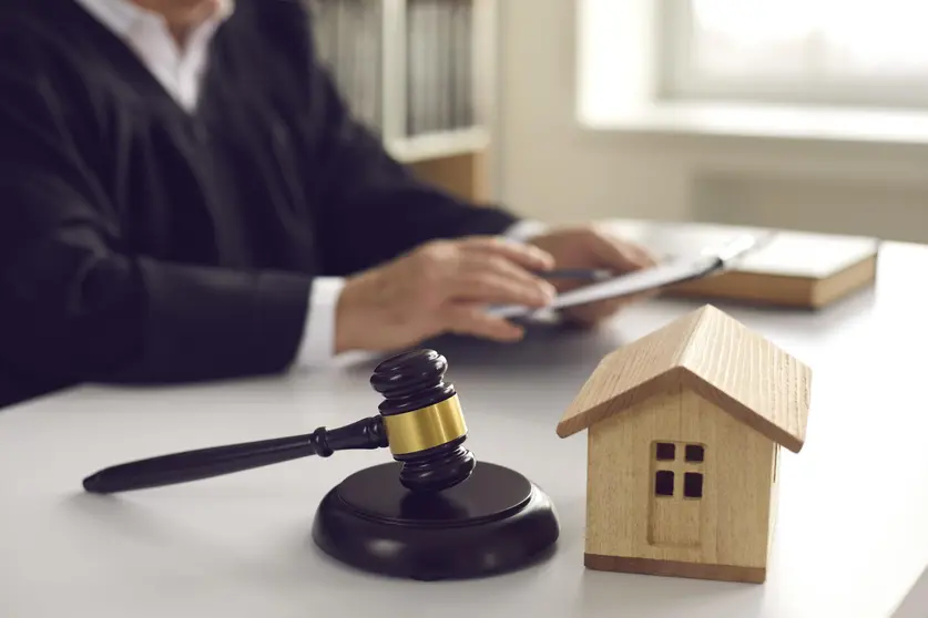 Brown gavel on sound block and small wooden house model on judge's table in courtroom during court hearing. Concept of real estate law, partition of property, separation of estates, divorce settlement