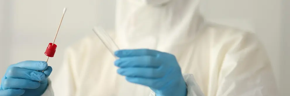 Doctor in protective suit holding test tube and cotton swab in clinic. Diagnostics covid-19 concept