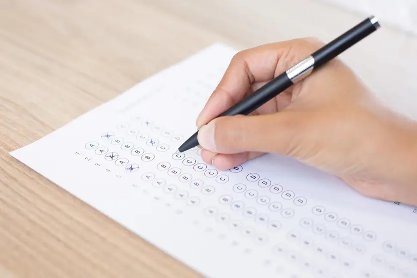 Closeup of hand holding pen and filling out questionary form on table