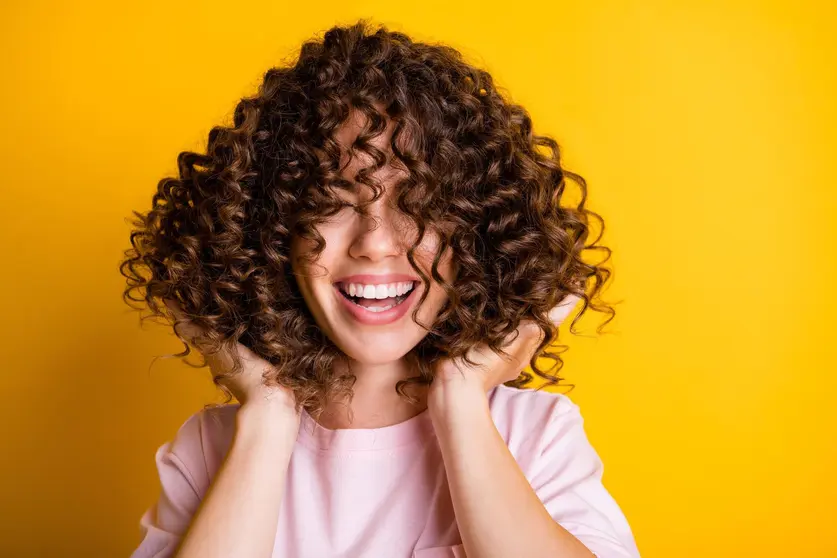 Photo portrait of girl with curly hairstyle wearing t-shirt laughing touching hair isolated on bright yellow color background.