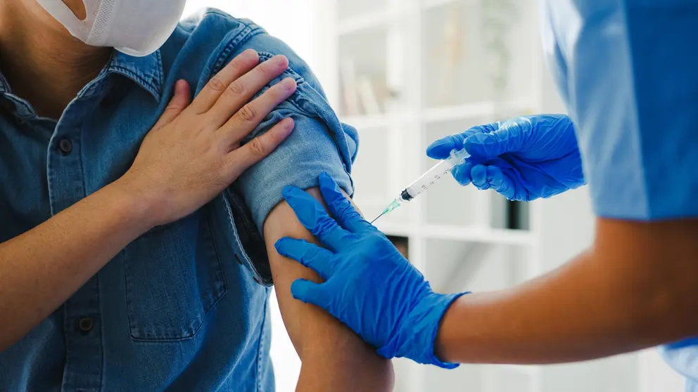 Young Asia lady nurse giving Covid-19 or flu antivirus vaccine shot to senior male patient wear face mask protection from virus disease at health clinic or hospital office. Vaccination concept.