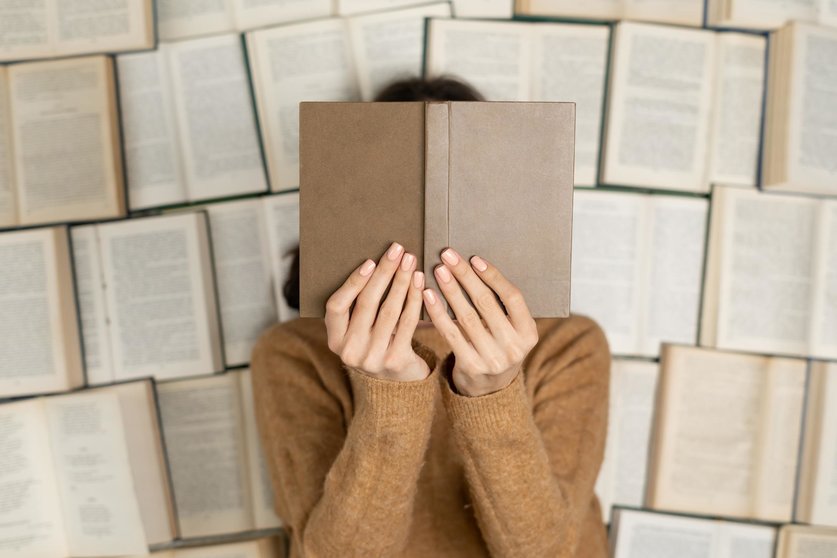 Top view, a girl in a cozy soft sweater lies on open books