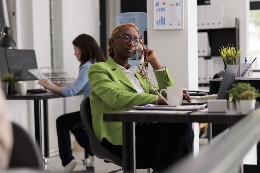 Employee having remote conversation with colleagues on landline phone, working in start up company coworking space. Office worker answering call, discussing financial strategy with business partners